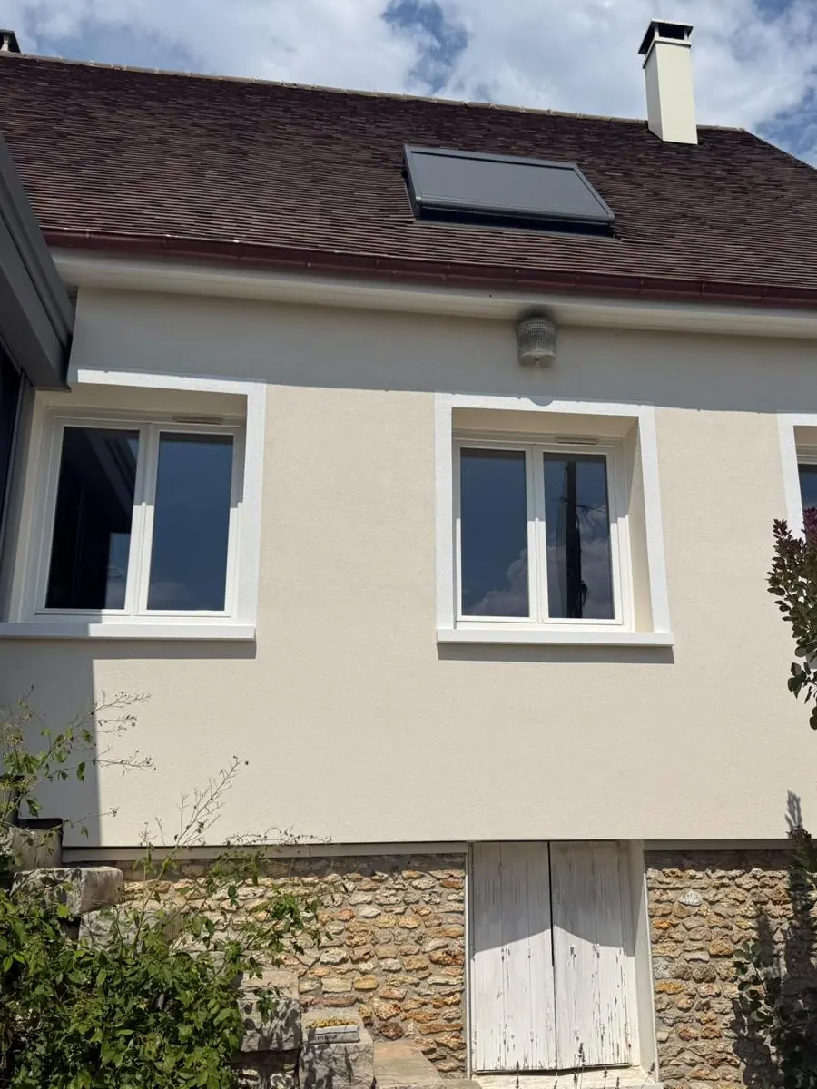 Façade d'une maison individuelle après remplacement des fenêtres PVC blanches, soubassement en pierre