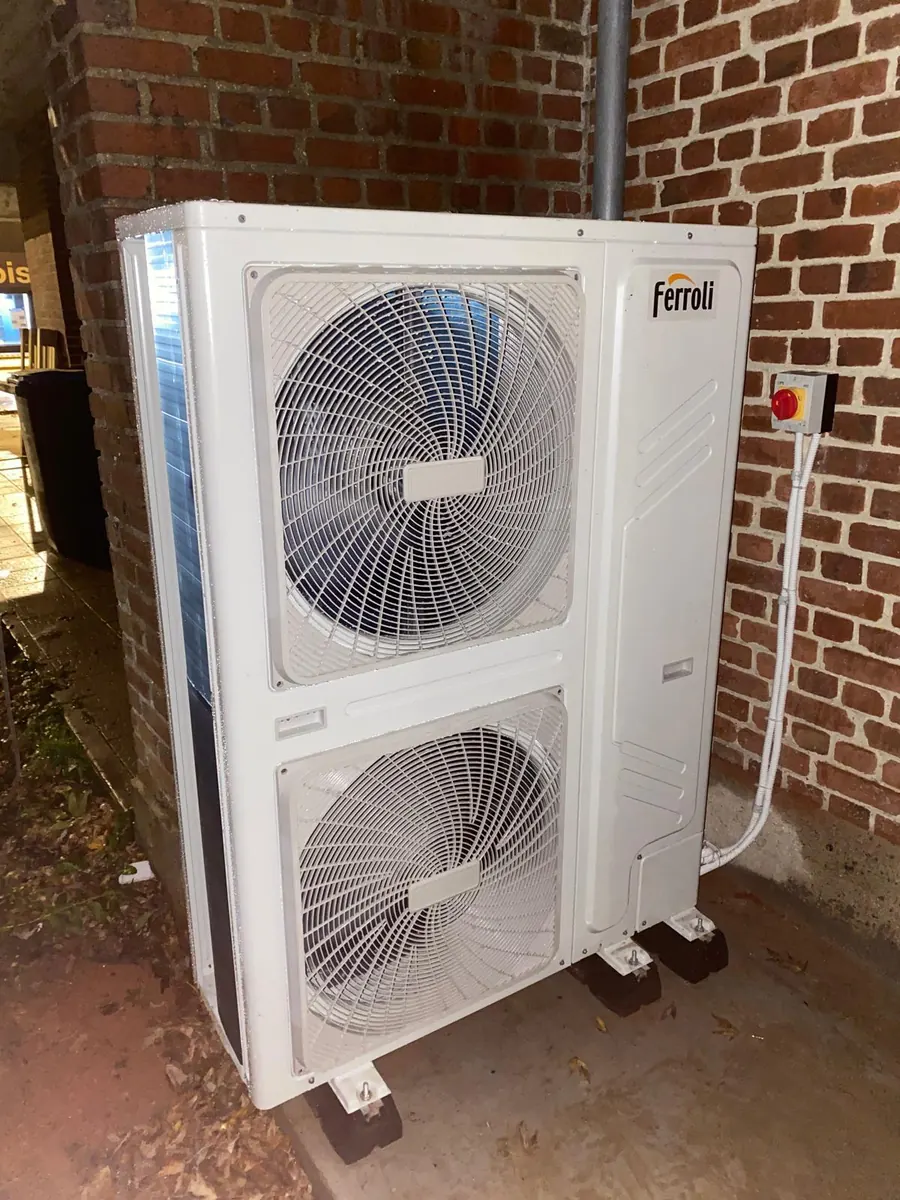 Unité extérieure de pompe à chaleur air/eau à deux ventilateurs installée contre un mur en brique